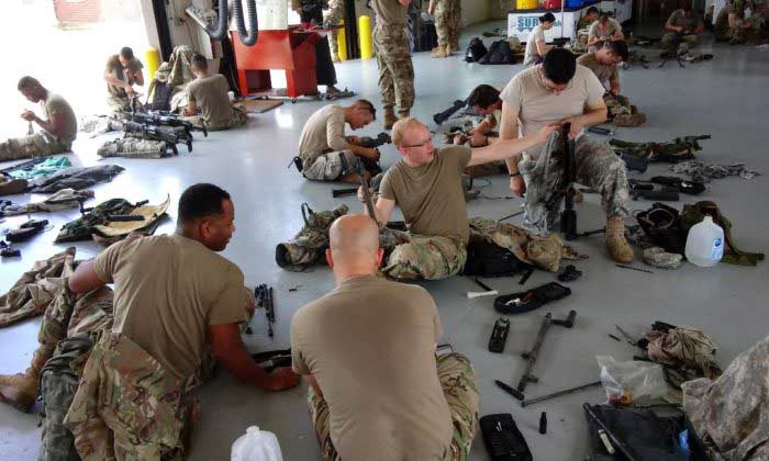 Group of soldiers sitting on floor cleaning rifles, machine guns, weapons maintenance